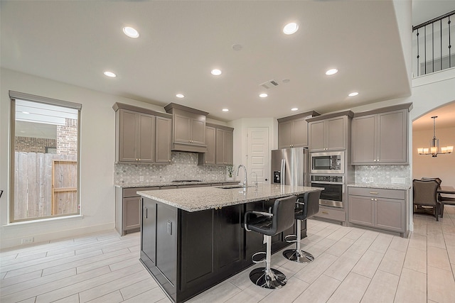 kitchen featuring a kitchen bar, a center island with sink, sink, gray cabinets, and appliances with stainless steel finishes