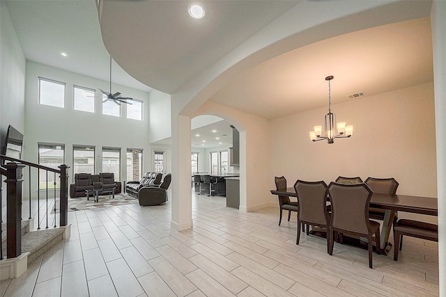 dining area featuring ceiling fan with notable chandelier, light hardwood / wood-style flooring, and a high ceiling