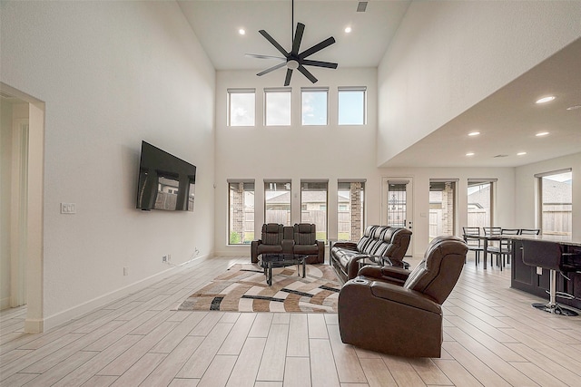 living room featuring ceiling fan, light hardwood / wood-style floors, and a towering ceiling