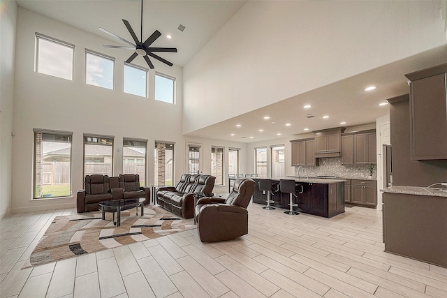 living room with light wood-type flooring, a wealth of natural light, ceiling fan, and a high ceiling