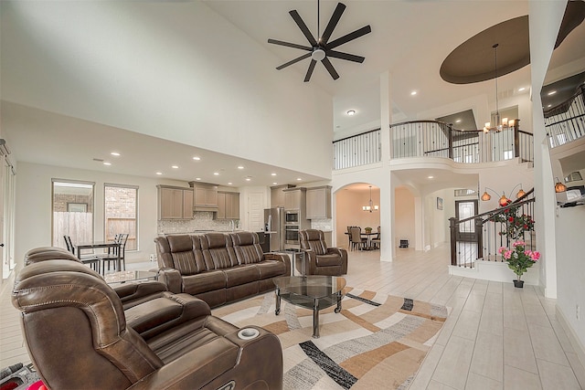 living room featuring ceiling fan with notable chandelier, light hardwood / wood-style floors, and a high ceiling