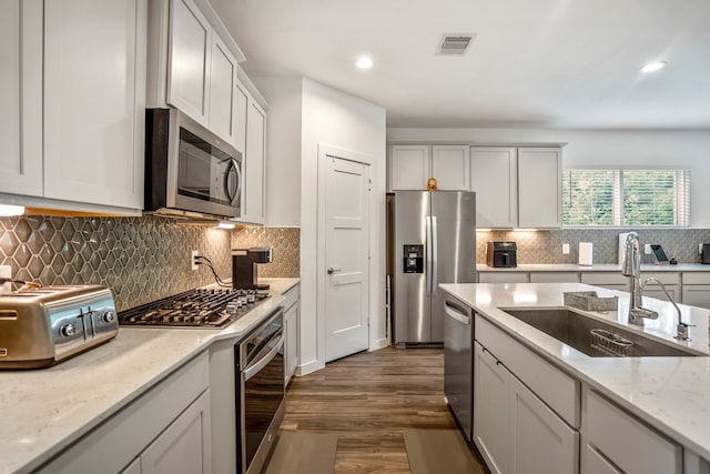 kitchen with tasteful backsplash, stainless steel appliances, light stone countertops, sink, and dark wood-type flooring