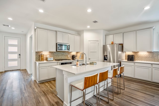 kitchen featuring tasteful backsplash, a center island with sink, light wood-type flooring, appliances with stainless steel finishes, and sink