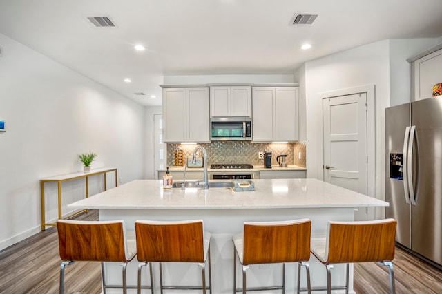 kitchen with white cabinetry, light hardwood / wood-style floors, appliances with stainless steel finishes, and a center island with sink