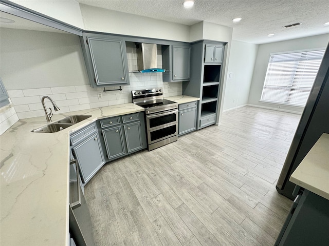 kitchen with double oven range, light stone counters, wall chimney exhaust hood, sink, and tasteful backsplash