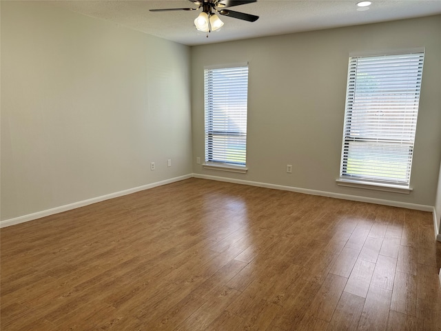 spare room featuring ceiling fan, hardwood / wood-style floors, and a healthy amount of sunlight