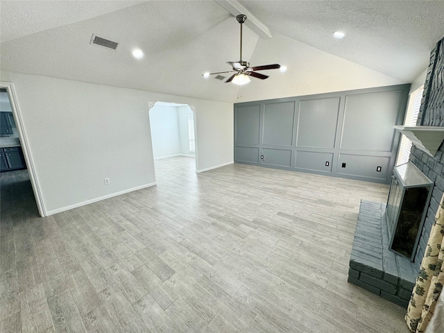 unfurnished living room with lofted ceiling with beams, ceiling fan, a brick fireplace, and light hardwood / wood-style flooring