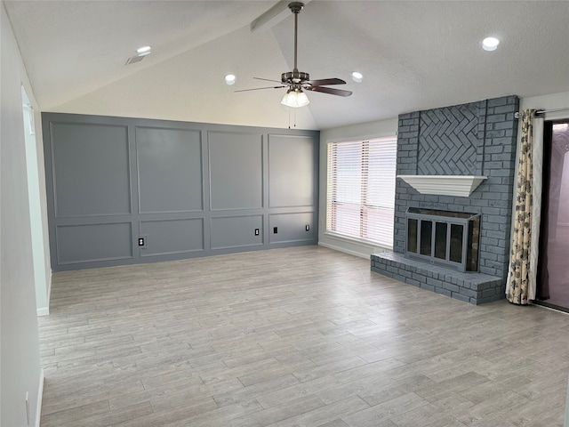 unfurnished living room with a brick fireplace, lofted ceiling, a textured ceiling, ceiling fan, and light hardwood / wood-style flooring