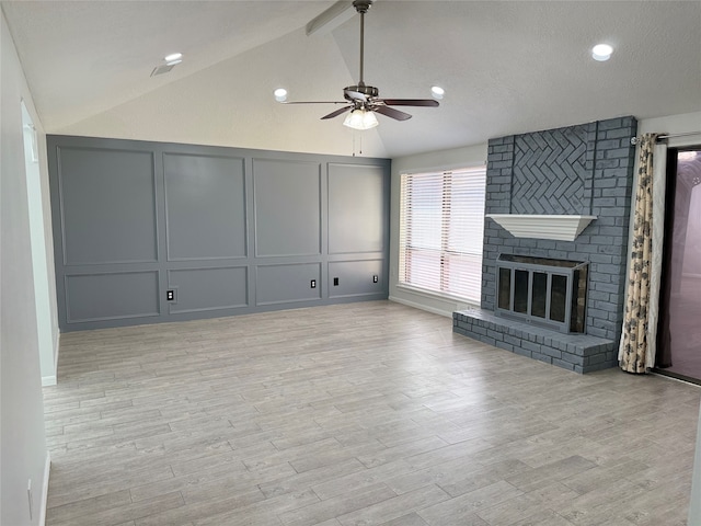 unfurnished living room featuring a brick fireplace, light hardwood / wood-style floors, lofted ceiling, a textured ceiling, and ceiling fan