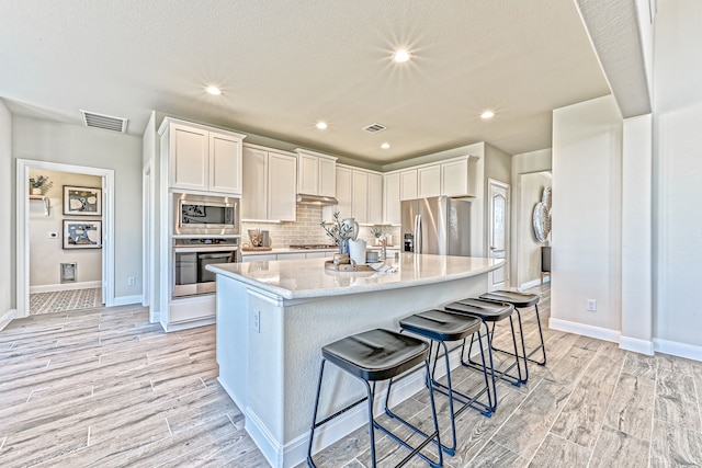 kitchen featuring a center island with sink, white cabinets, light wood-type flooring, and stainless steel appliances