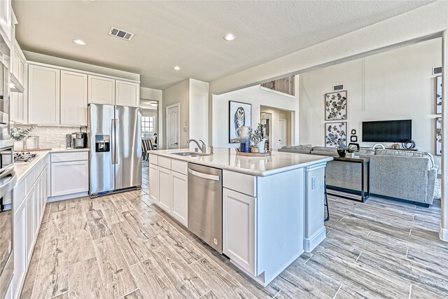 kitchen featuring white cabinetry, sink, a center island with sink, light wood-type flooring, and stainless steel appliances