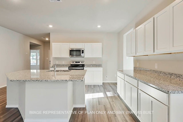 kitchen featuring a kitchen island with sink, stainless steel appliances, light stone countertops, white cabinets, and light hardwood / wood-style flooring