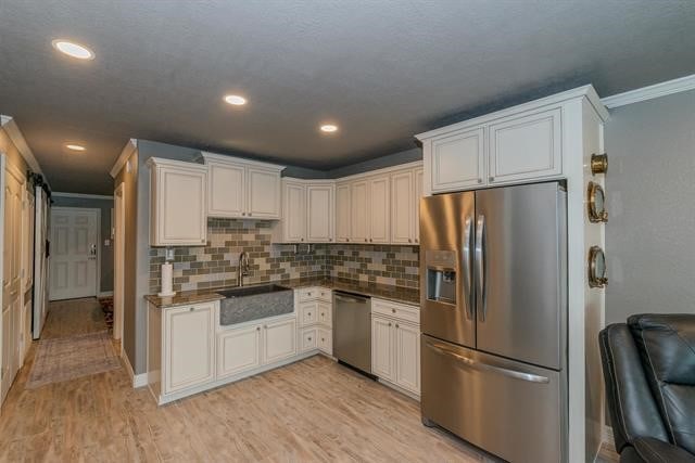 kitchen featuring ornamental molding, stainless steel appliances, backsplash, sink, and light hardwood / wood-style flooring