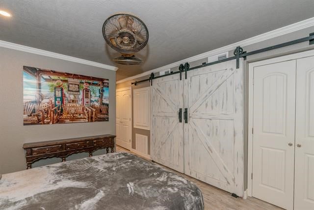 bedroom featuring ornamental molding, light wood-type flooring, a barn door, and a closet