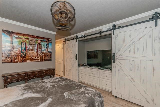 bedroom featuring a barn door, a textured ceiling, light wood-type flooring, and crown molding