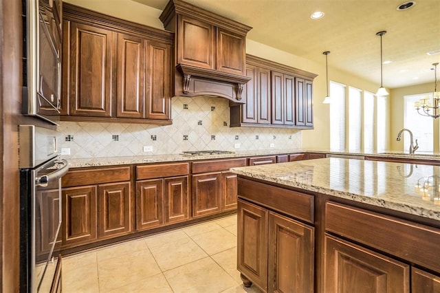 kitchen featuring light stone countertops, backsplash, sink, pendant lighting, and a chandelier