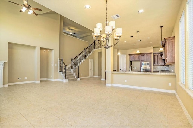 unfurnished living room featuring sink, a towering ceiling, ceiling fan with notable chandelier, and light tile patterned flooring