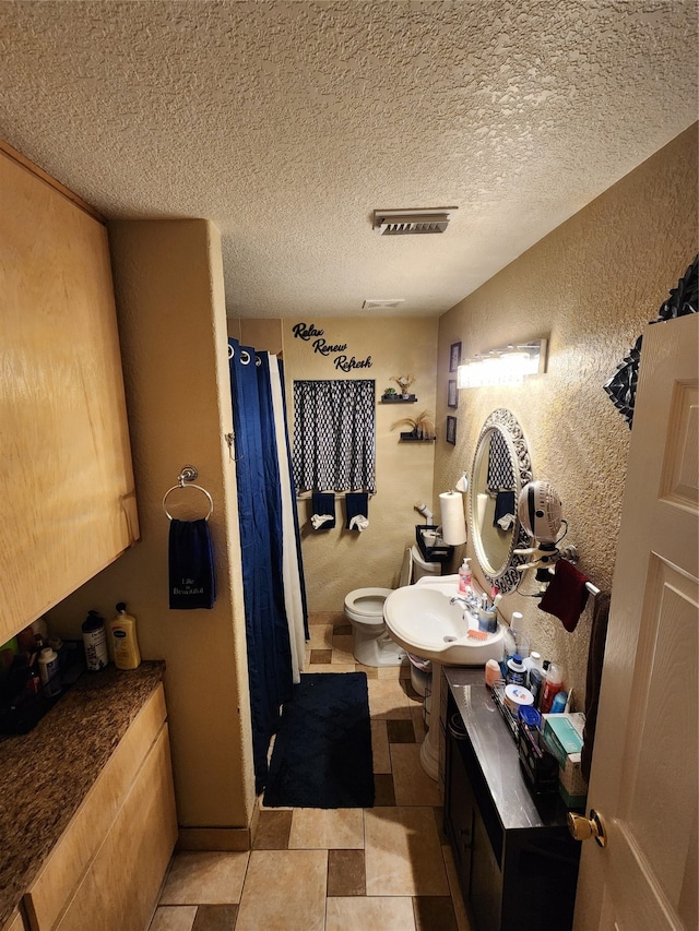 bathroom featuring a shower with shower curtain, a textured ceiling, vanity, tile patterned floors, and toilet