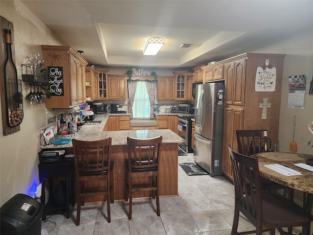 kitchen with stainless steel appliances, sink, kitchen peninsula, a kitchen bar, and a tray ceiling