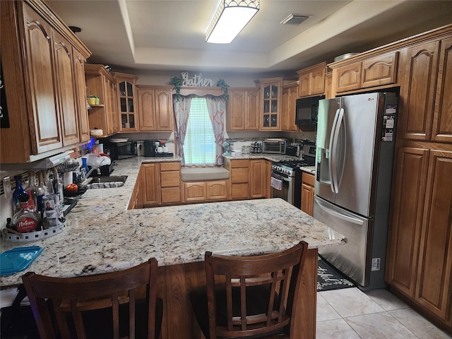 kitchen with stainless steel appliances, light stone counters, kitchen peninsula, a kitchen breakfast bar, and a raised ceiling