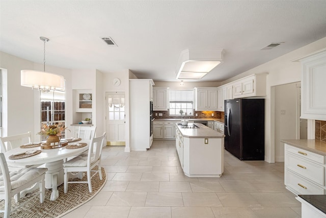 kitchen featuring tasteful backsplash, black fridge, a notable chandelier, decorative light fixtures, and white cabinets