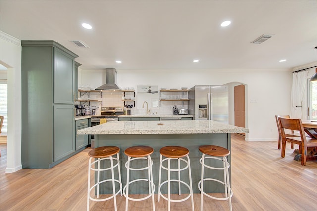 9932 Shady Dr, Houston, TX 77016 - kitchen with wall chimney range hood, green cabinets, appliances with stainless steel finishes, a sink, and arched walkways