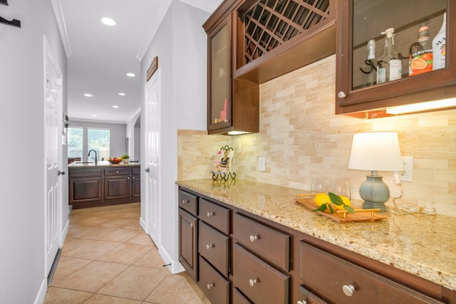 kitchen featuring light tile patterned flooring, light stone counters, ornamental molding, and sink