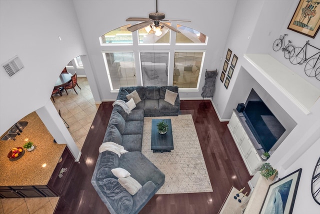 living room featuring ceiling fan, a towering ceiling, and dark wood-type flooring