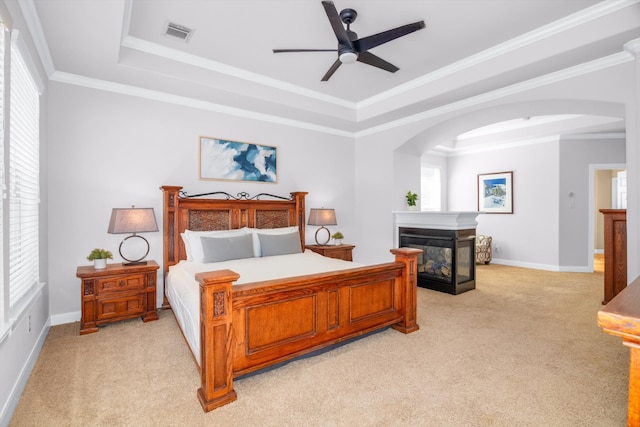 carpeted bedroom with a multi sided fireplace, a tray ceiling, and crown molding