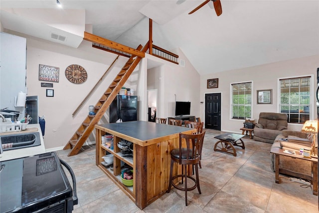 kitchen featuring ceiling fan, black fridge, sink, a kitchen breakfast bar, and high vaulted ceiling