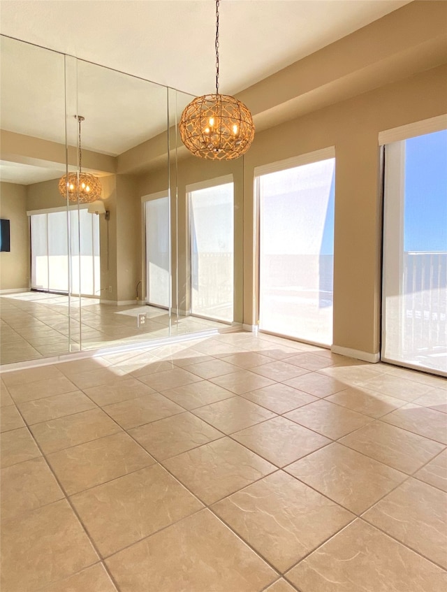 tiled empty room featuring a wealth of natural light and a notable chandelier