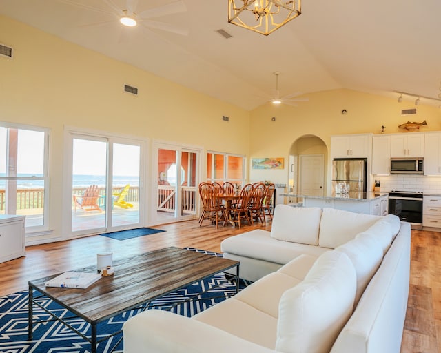 living room featuring ceiling fan with notable chandelier, light wood-type flooring, and high vaulted ceiling