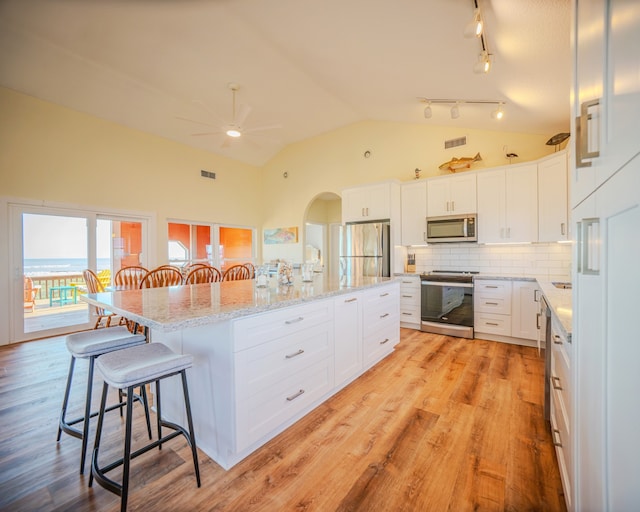 kitchen with a kitchen bar, stainless steel appliances, light hardwood / wood-style floors, an island with sink, and white cabinetry