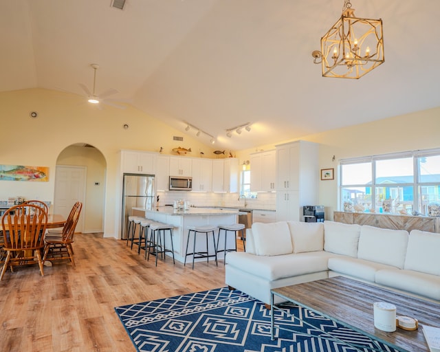 living room with high vaulted ceiling, ceiling fan with notable chandelier, and light hardwood / wood-style flooring