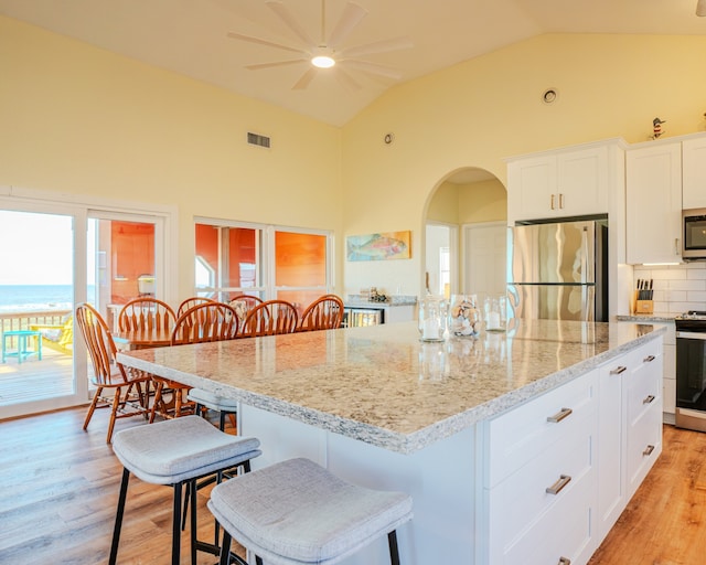 kitchen with appliances with stainless steel finishes, a breakfast bar area, a center island, and light hardwood / wood-style flooring