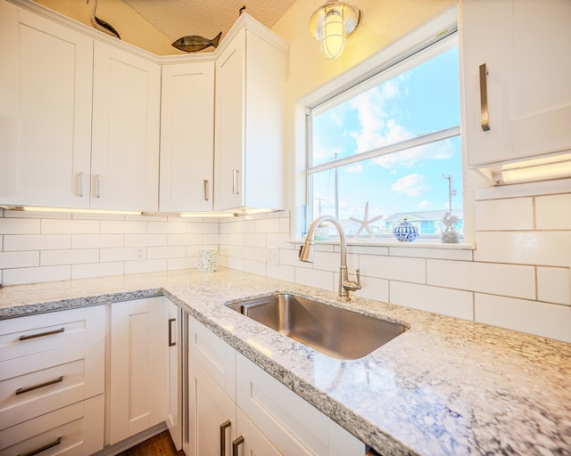 kitchen featuring light stone counters, white cabinets, a textured ceiling, sink, and backsplash