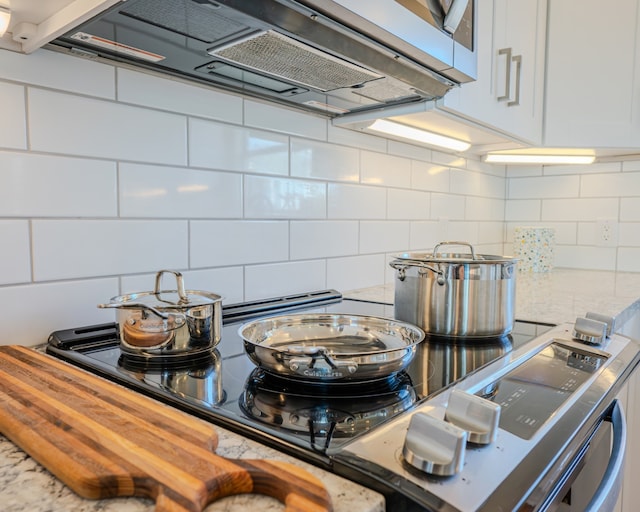 interior details with wooden counters, white cabinetry, range hood, and backsplash