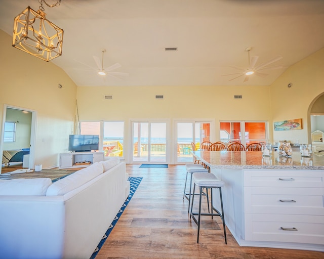 living room with high vaulted ceiling, light hardwood / wood-style flooring, and ceiling fan with notable chandelier