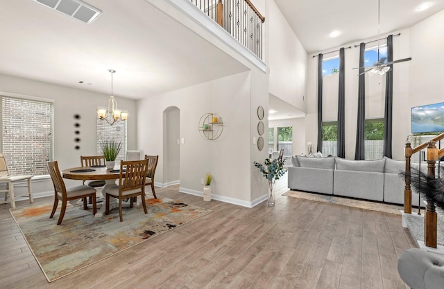 dining room with a towering ceiling, light hardwood / wood-style floors, and ceiling fan with notable chandelier