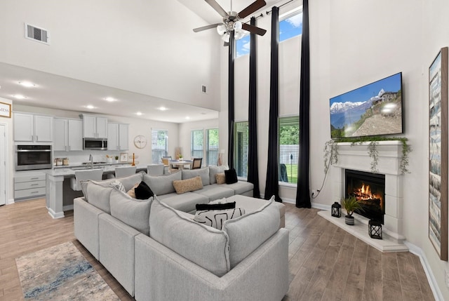 living room featuring a towering ceiling, ceiling fan, sink, and light hardwood / wood-style floors