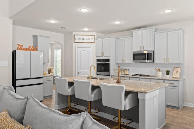 kitchen with stainless steel appliances, light wood-type flooring, light stone countertops, sink, and a kitchen island with sink