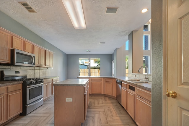 kitchen with a center island, sink, a textured ceiling, appliances with stainless steel finishes, and kitchen peninsula