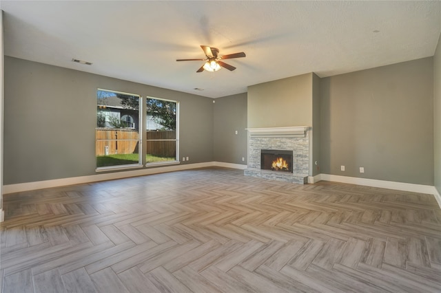 unfurnished living room with a textured ceiling, light parquet flooring, a stone fireplace, and ceiling fan