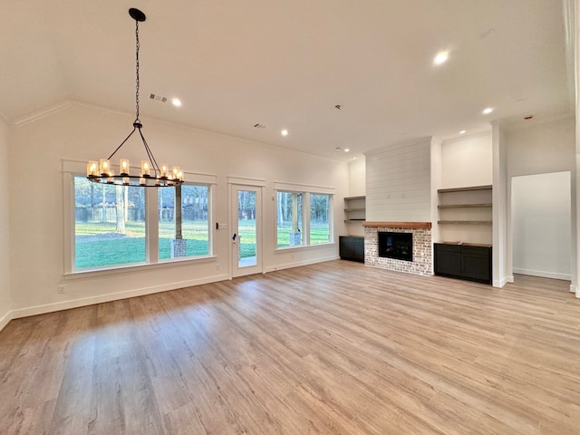 unfurnished living room with a brick fireplace, light hardwood / wood-style floors, an inviting chandelier, and crown molding