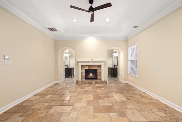 unfurnished living room featuring ceiling fan, a tile fireplace, crown molding, and a tray ceiling