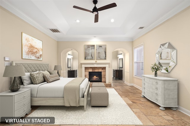 bedroom with a tiled fireplace, ceiling fan, crown molding, and a tray ceiling