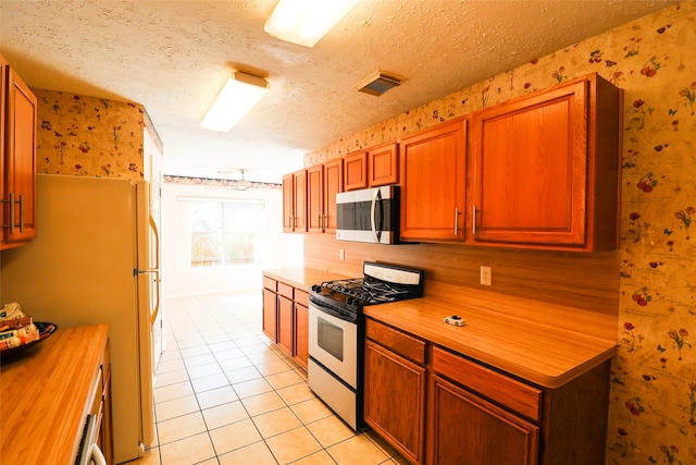 kitchen with refrigerator, light tile patterned flooring, a textured ceiling, and white gas range oven