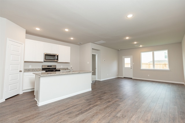 kitchen featuring wood-type flooring, white cabinets, an island with sink, light stone countertops, and appliances with stainless steel finishes