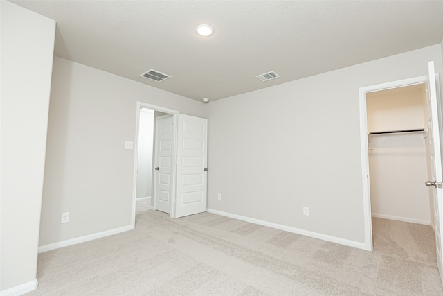 unfurnished bedroom with a closet, a spacious closet, and light colored carpet