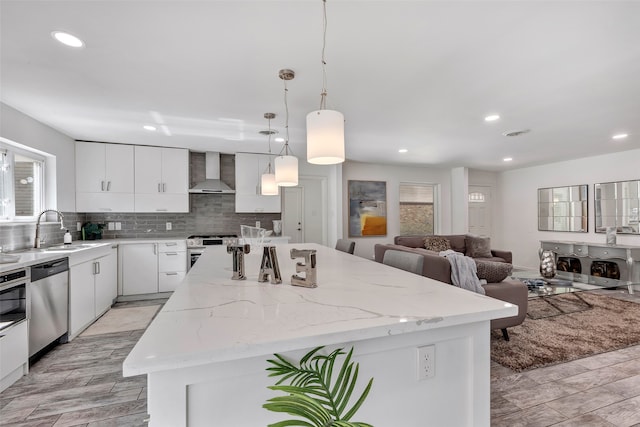 kitchen featuring appliances with stainless steel finishes, wall chimney exhaust hood, sink, pendant lighting, and a kitchen island